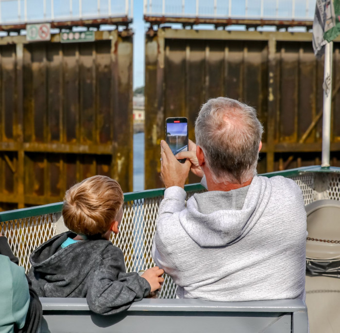 Dad and son on deck of the tour boat Holiday taking photos of the lock gates opening during a classic Original Soo Locks Boat Tours.