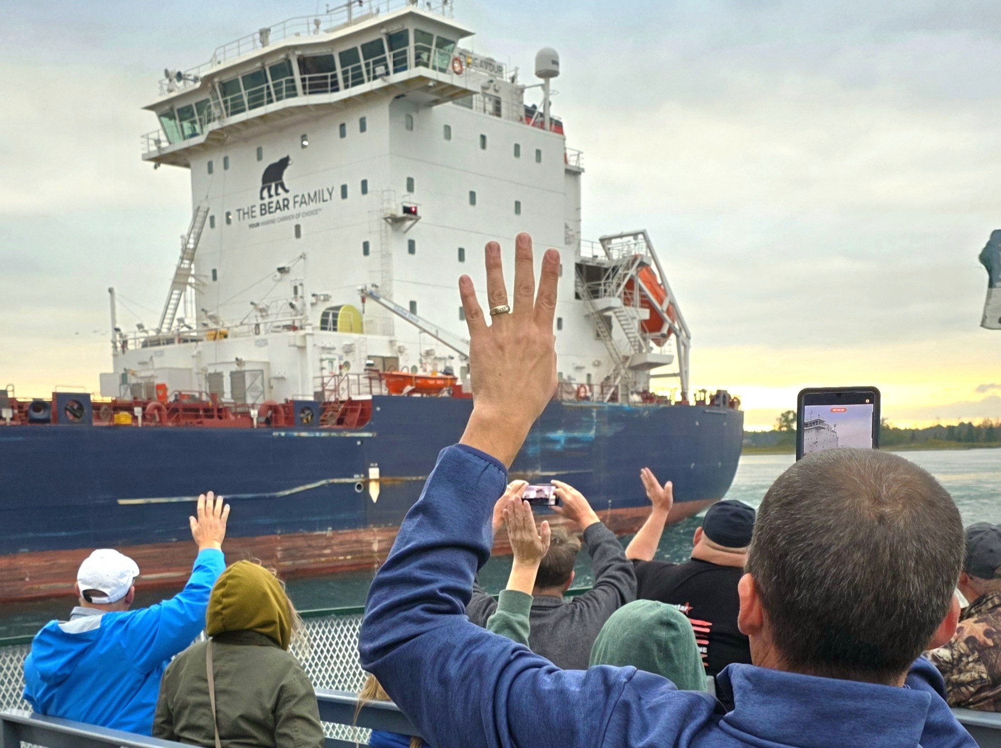 Guest waving to a Great Lakes freighter during a master salute on an Original Soo Locks Boatnerd Cruise, a family fun event in Michigan’s Upper Peninsula