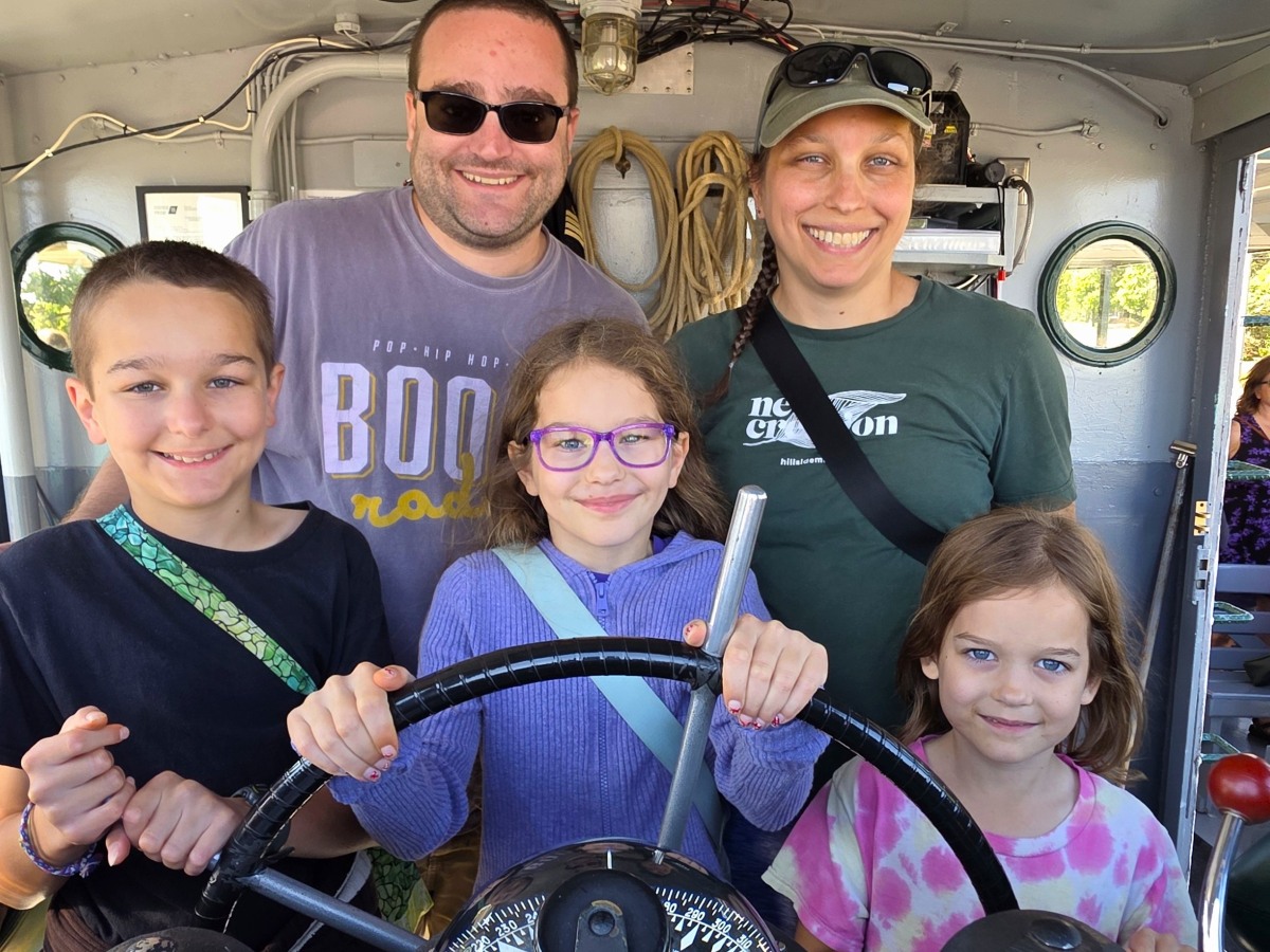 Children standing at the wheel inside the pilot house during an interactive moment on a Soo Locks boat tour, offering a fun hands-on experience for families.