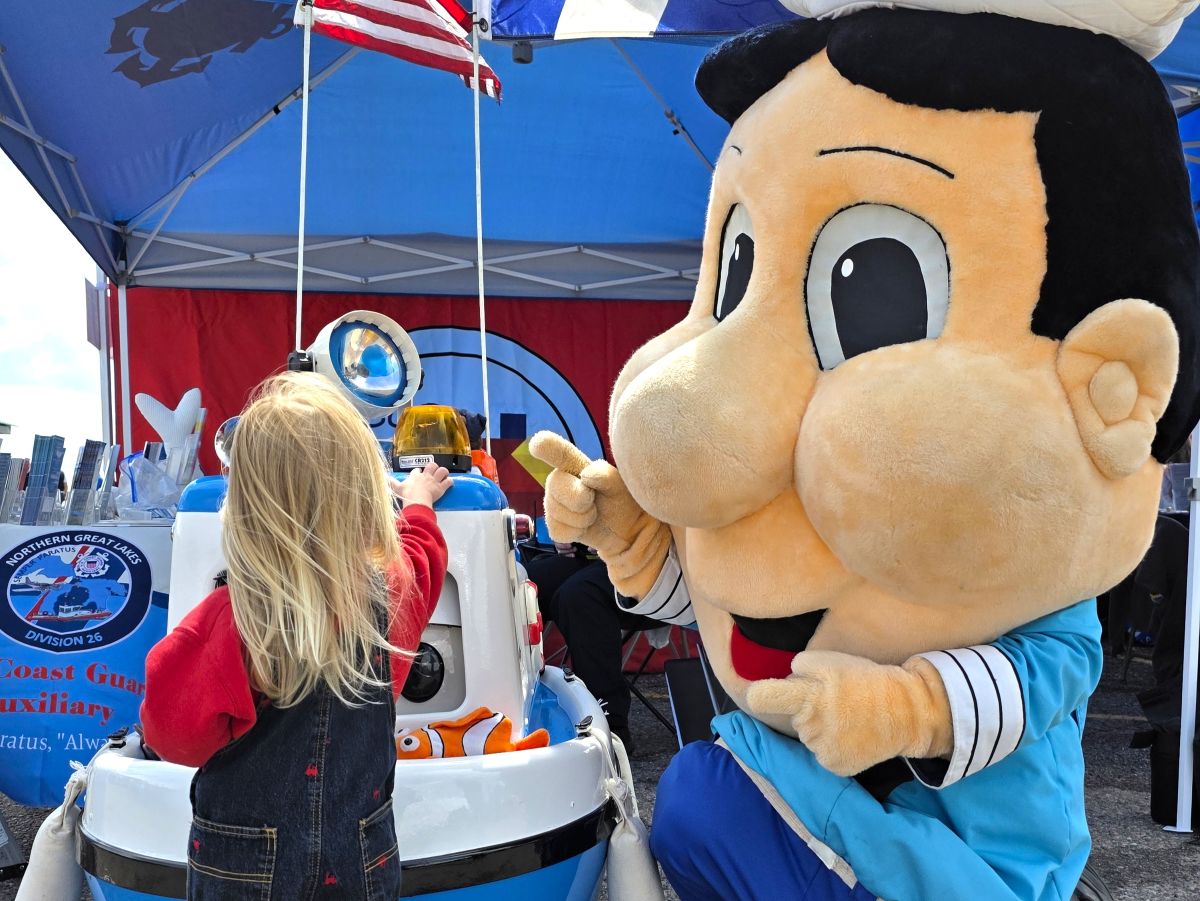A young child interacting with a Coast Guard–themed display alongside a friendly mascot Decky during Little Sailors Day, a family‑friendly maritime event at the Soo Locks in Sault Ste. Marie, Michigan.
