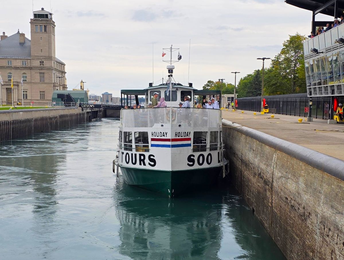 The Soo Locks tour boat Holiday inside the lock chamber during a live lock-through in Sault Ste. Marie, Michigan, with the historic Administration Building in the background.