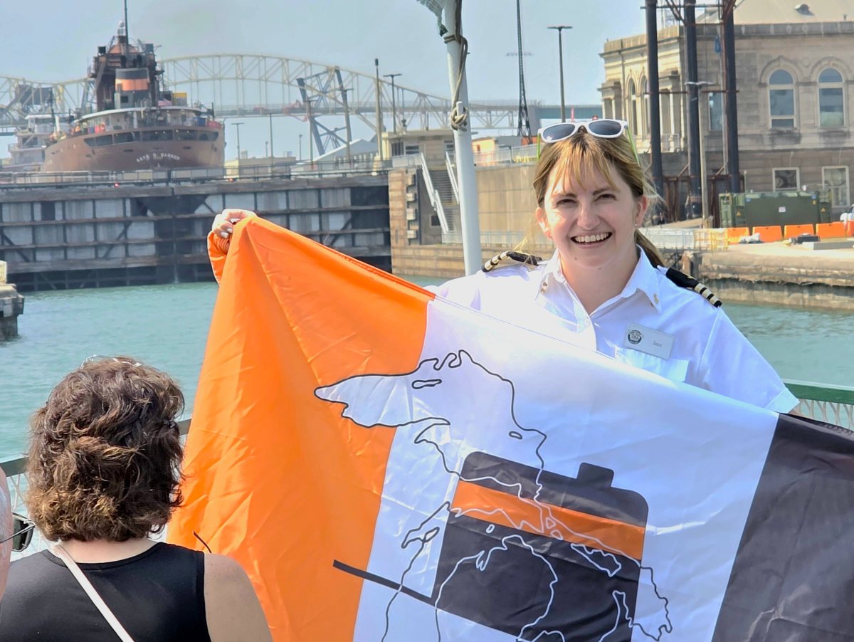 crew from the Original Soo Locks Boat Tours holding an Interlake Steamship Company Fag with the freighter Key E. Barker locking up the Soo Locks on a Michigan's Upper Peninsula lock tour.